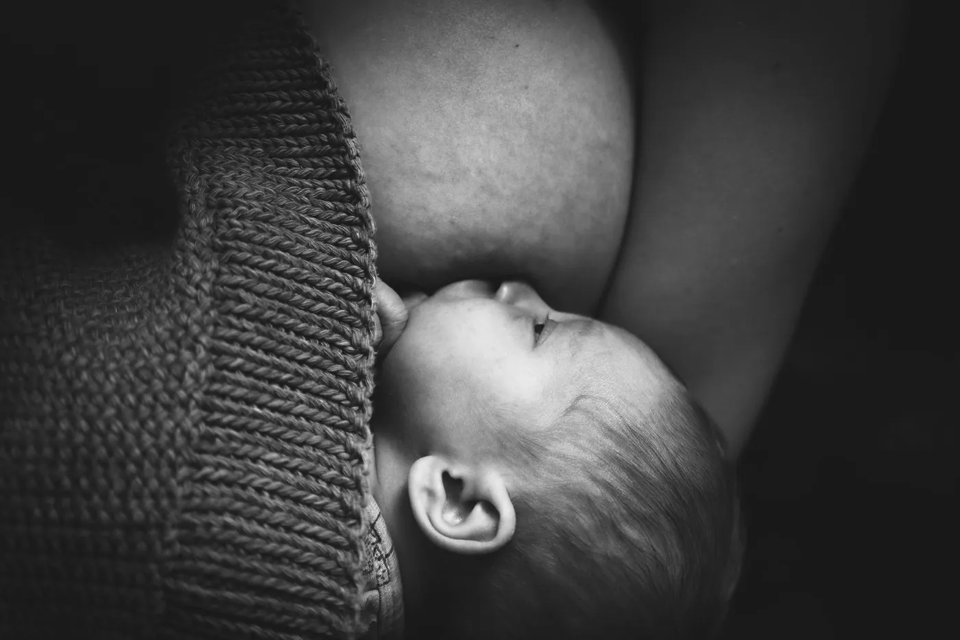 Photo en noir et blanc : un nouveau-né tète, blotti contre sa mère.
