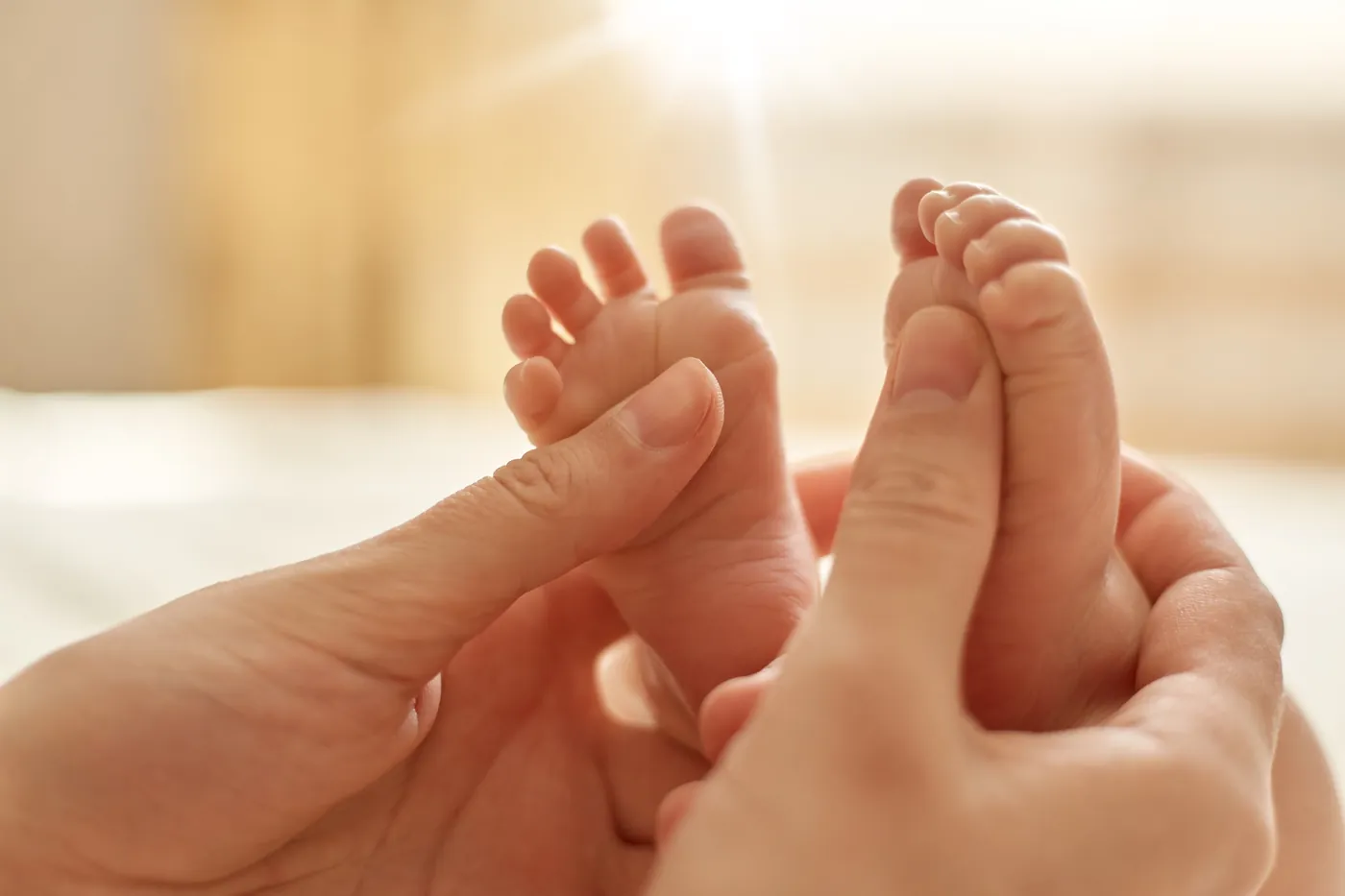 Des mains d'adulte tiennent et massent les petits pieds d'un bébé.